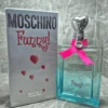 Perfume original Moschino Funny! para mujer en frasco azulado con tapón de corazón plateado, lazo rosa y caja original.