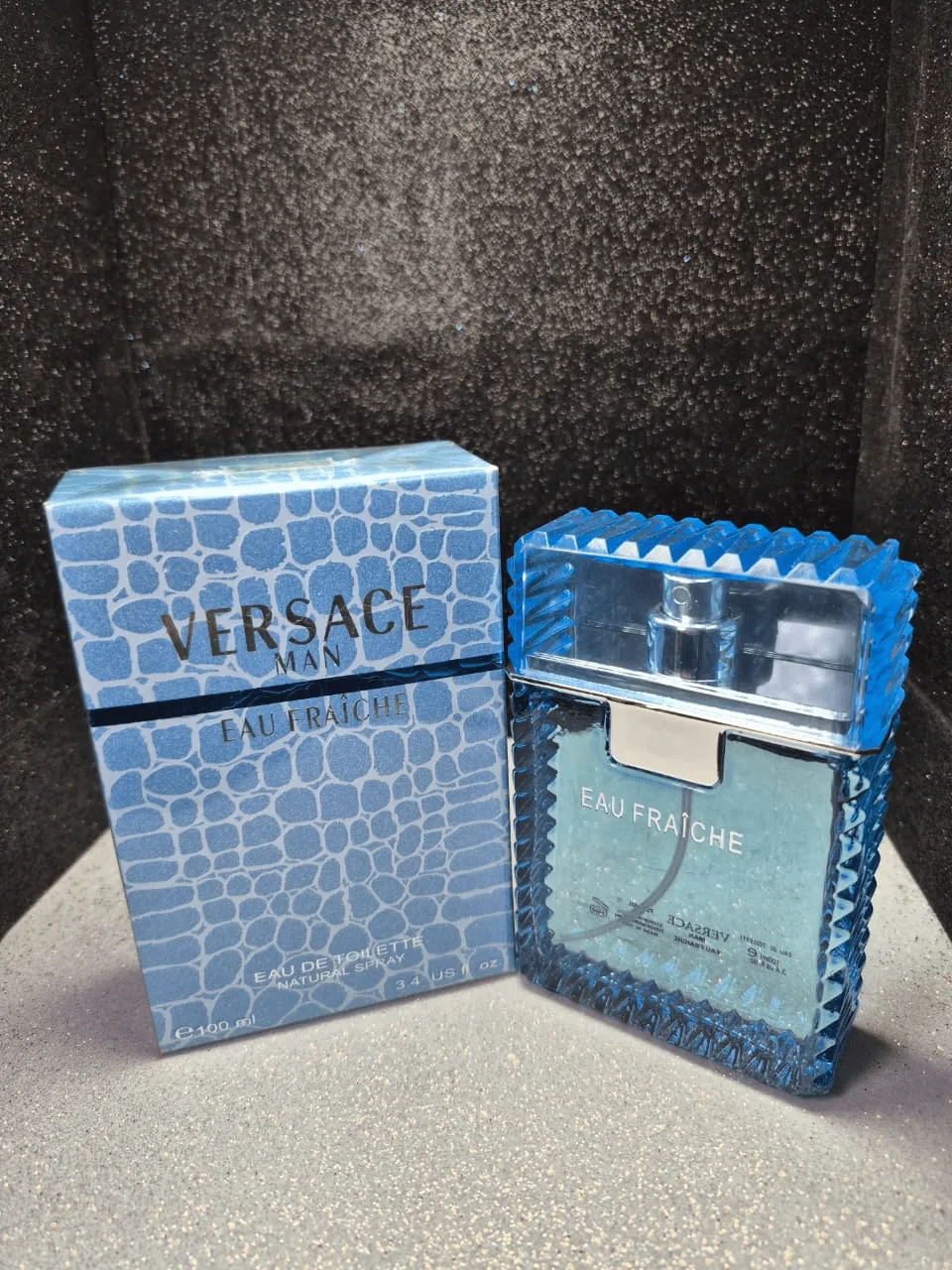 Perfume original Versace Man Eau Fraiche para hombre en frasco azul claro con bordes dentados y caja original.
